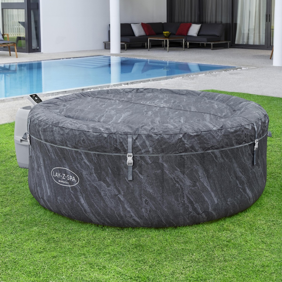 Jacuzzi z nałożoną ciemnoszarą, wzmocnioną pokrywą zabezpieczoną klamrami. Produkt stoi na zielonym trawniku obok nowoczesnego domu z basenem.